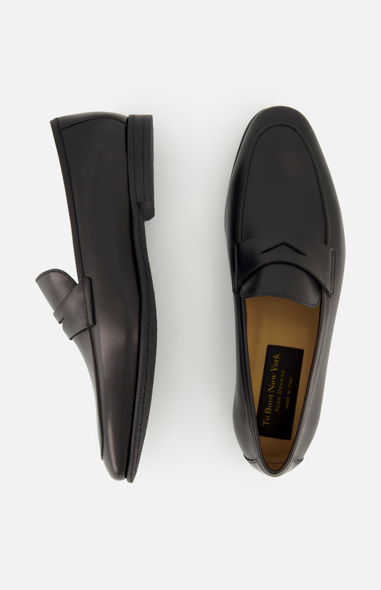 The Keats Leather Penny Loafer by TO BOOT is displayed, with one black leather shoe viewed from the side and the other from above. A tan inner sole featuring a visible TO BOOT brand label highlights these classic slip-on dress shoes.