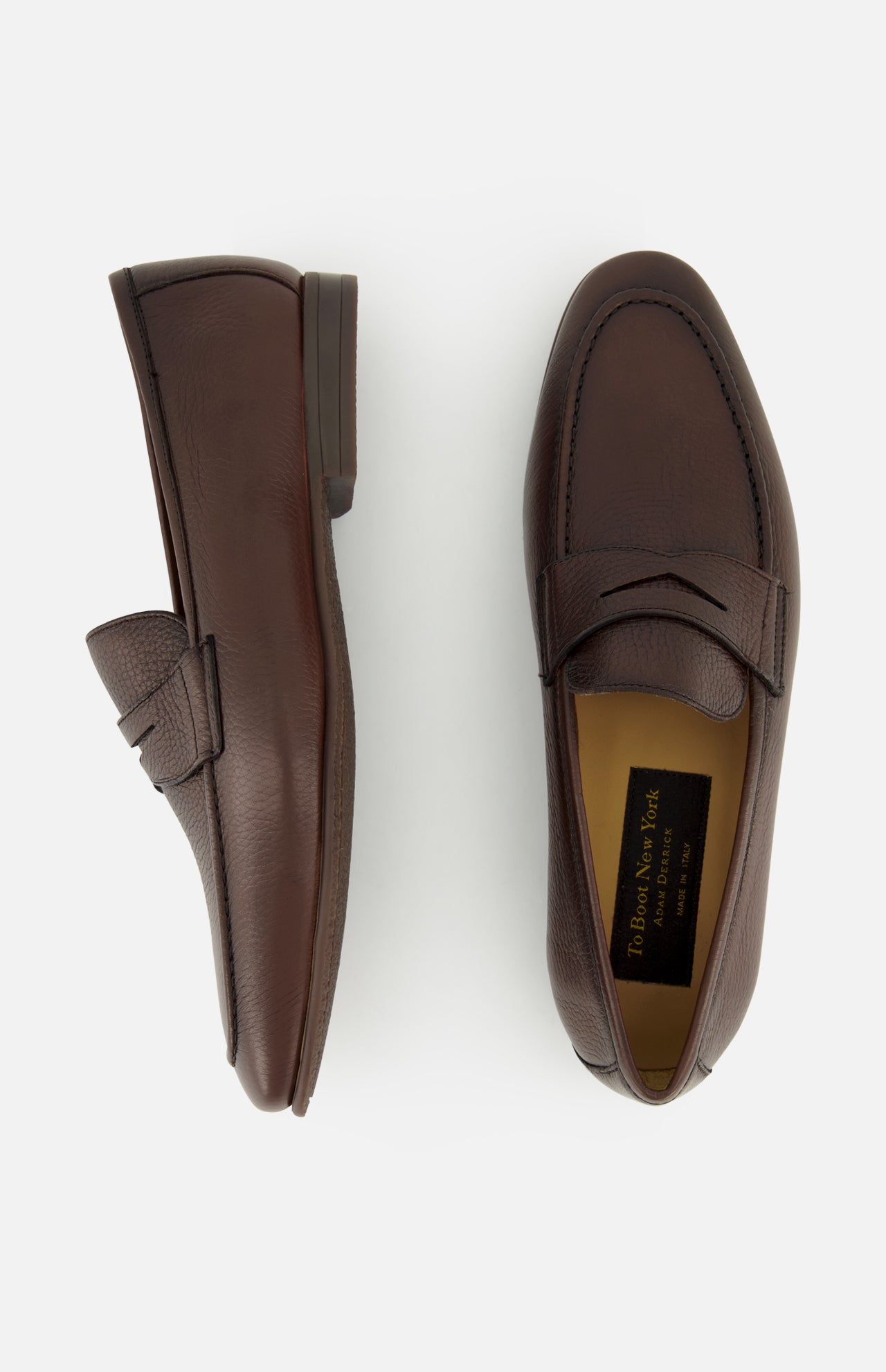 The TO BOOT Merritt Deer Leather Penny Loafer, showcased here in brown Italian deer leather, features one shoe displayed from the side and the other from above against a plain white background. This classic penny loafer design embodies timeless elegance and sophistication.