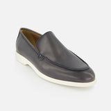 The TO BOOT Pacific Leather Hybrid Loafer is a black slip-on men's shoe with a white rubber sole and minimalist design, photographed at an angle on a white background—ideal for a modern, lace-free dress look.