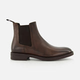 The Peabody Chelsea Boot by TO BOOT is a men’s brown grained leather boot with a black elastic side panel, back pull tab, and low heel, shown in profile on a white background.