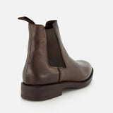 The Peabody Chelsea Boot by TO BOOT features brown grained leather, a rear pull tab, black elastic side panel, and dark sole—shown from a rear-side angle on white—perfect for fall.