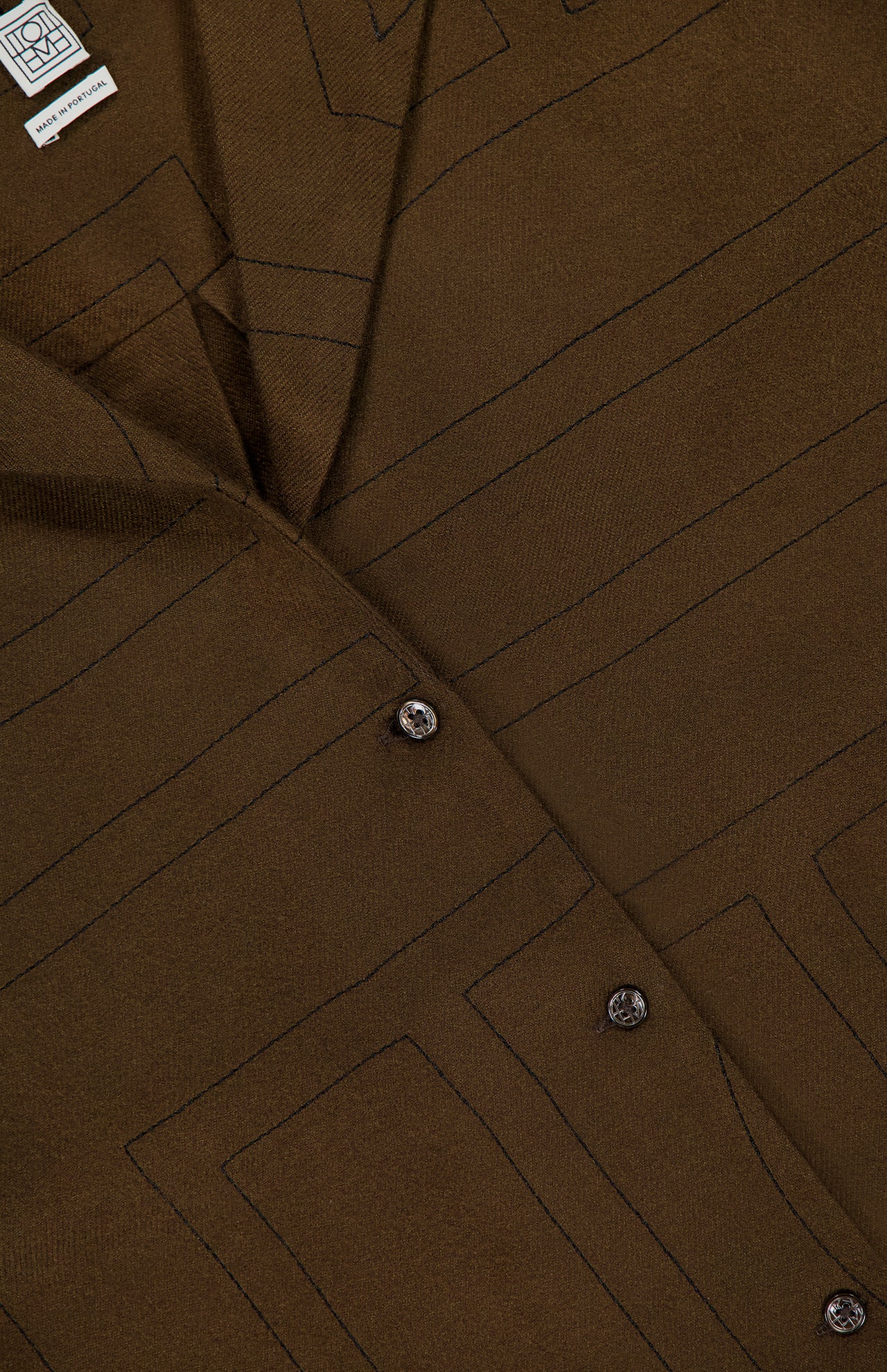 Close-up of TOTEME’s Monogram Flannel PJ Top in dark brown, featuring a geometric stitched pattern, four glossy buttons, and a small white label at the upper left—all highlighting its relaxed silhouette.