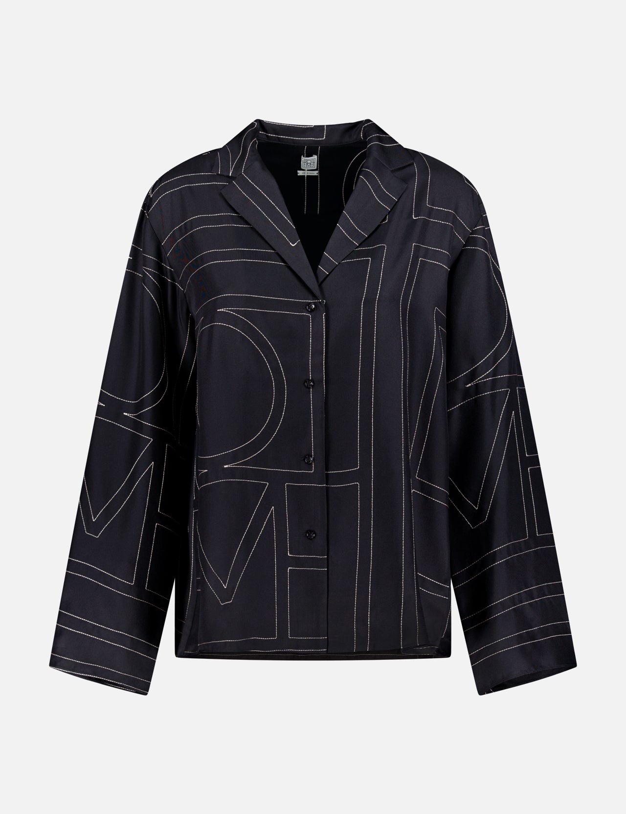 The TOTEME Monogram Silk PJ Top is a black, long-sleeve silk blouse with a boxy fit, geometric white line pattern, and notched collar—a modern designer piece displayed on a plain white background.