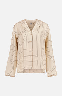 The TOTEME Monogram Silk PJ Top is a beige long-sleeve, wide-collar shirt featuring a dark brown abstract monogram print and relaxed fit, offering an elegant update to the classic ivory blouse.