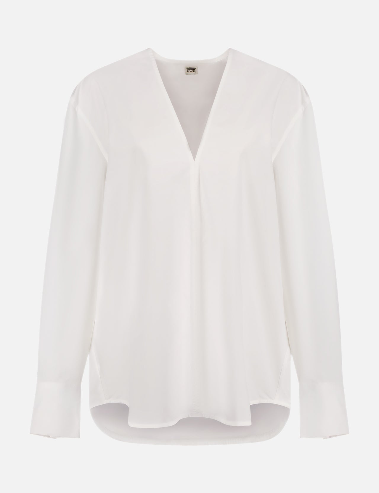 The TOTEME V-Neck Cotton Shirt is a white, minimalist blouse with a loose fit, slightly extended cuffs, and a curved hem that's longer in the back. It is displayed on a plain white background.