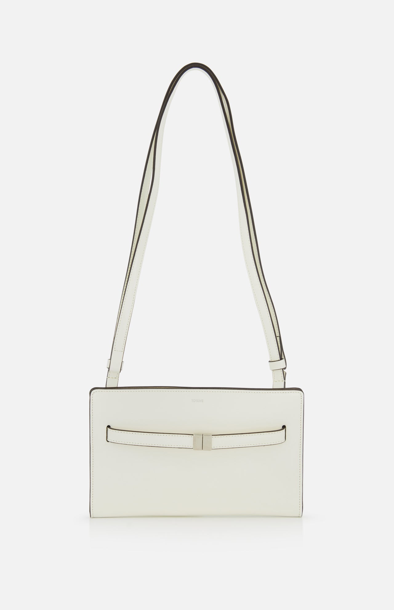 The TOTEME Belted Naplack Crossbody Bag is a minimalist white leather handbag with a long strap, subtle black trim, and a slim horizontal accent on the front. Made in Italy. Displayed against a plain white background.