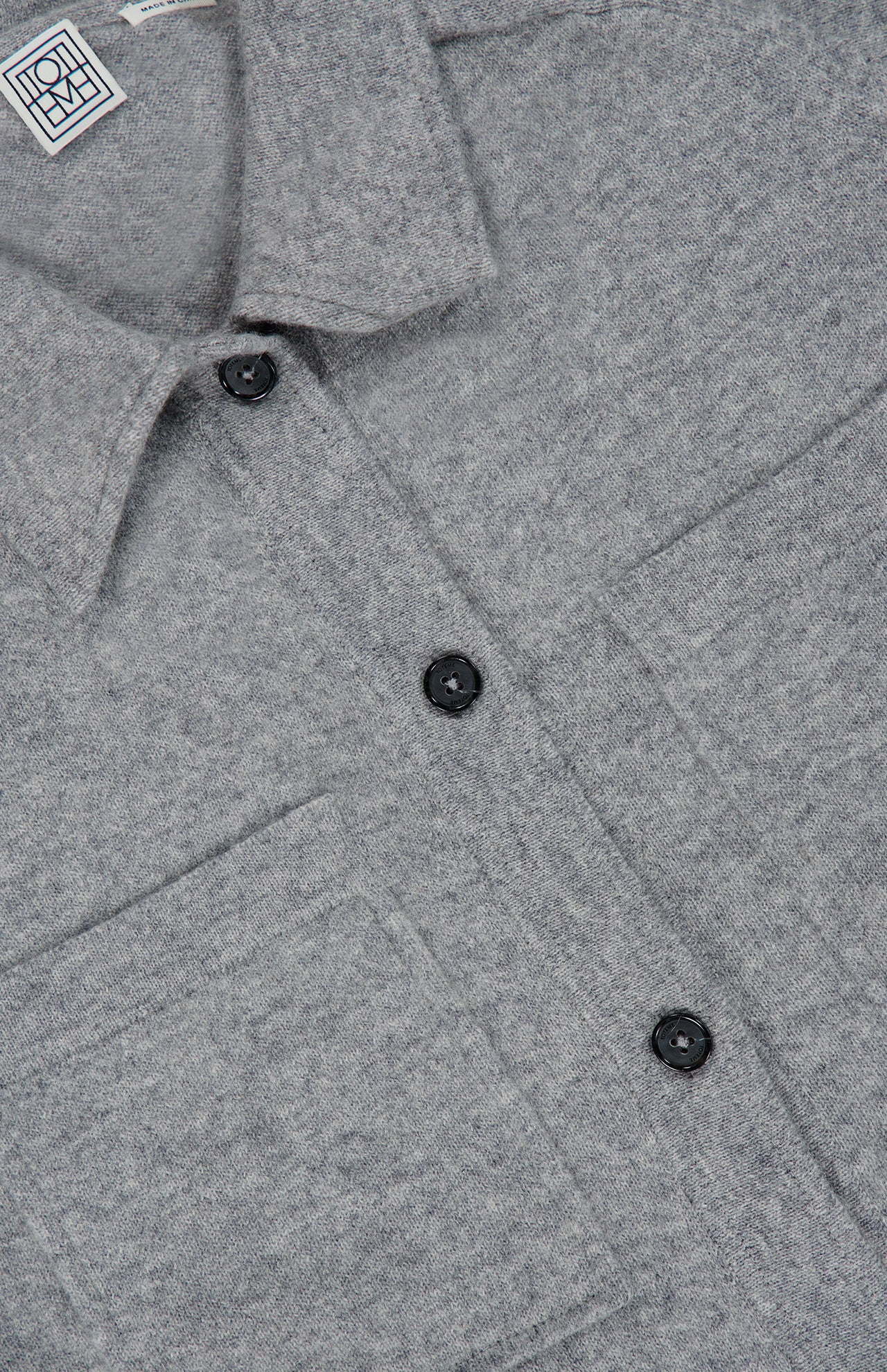 Close-up of the TOTEME Cashmere Long Sleeve Cardigan in grey, highlighting its button-front closure with black buttons, two chest pockets, classic collar, and the ultra-soft cashmere fabric texture.