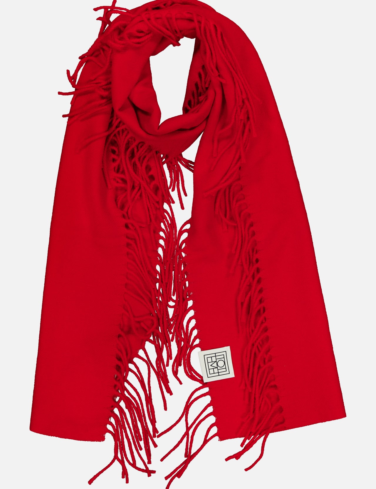 A vibrant TOTEME Wool and Cashmere Tassel Scarf in bright red, featuring fringed edges and a small white rectangular patch with a black geometric design, displayed on a white background. Expertly crafted in Italy, this luxurious scarf blends bold color with sophisticated style.