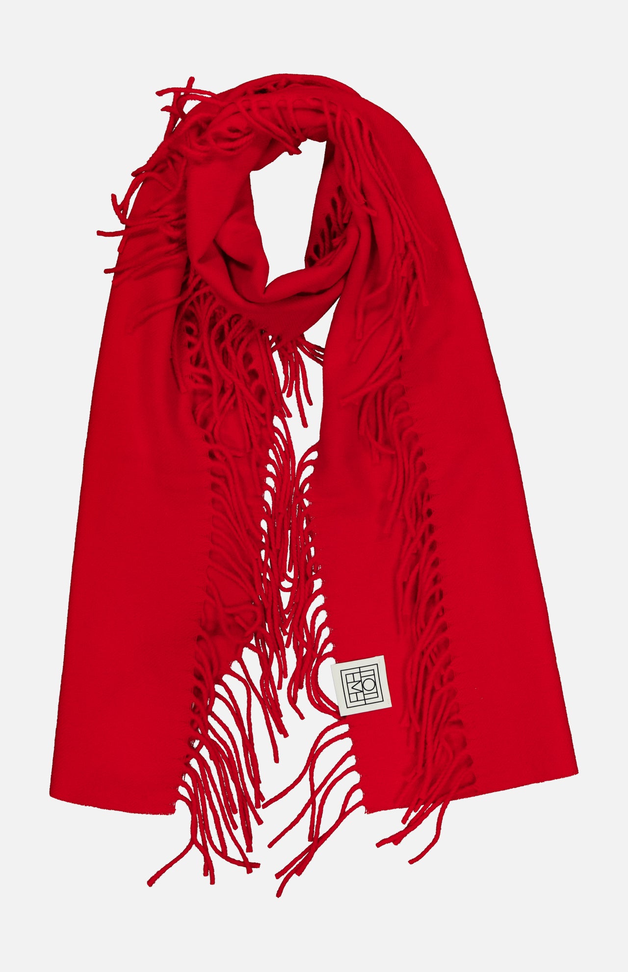 A vibrant TOTEME Wool and Cashmere Tassel Scarf in bright red, featuring fringed edges and a small white rectangular patch with a black geometric design, displayed on a white background. Expertly crafted in Italy, this luxurious scarf blends bold color with sophisticated style.