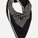 The TOTEME Centered Monogram Silk Scarf, featuring black silk adorned with white geometric stripes and borders, is elegantly arranged in a folded, slightly draped manner against a plain white background—a sophisticated women’s accessory perfect for elevating any look.