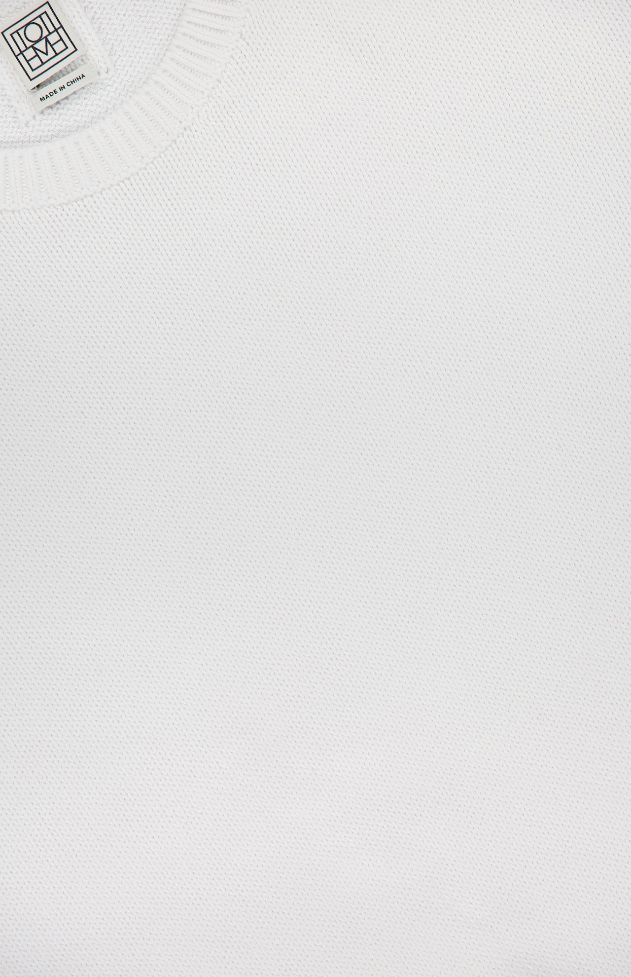 Close-up of the TOTEME Classic Cotton Crewneck Knit Sweater in plain white, featuring a visible collar and a small clothing label in the top left corner.