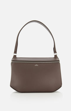 The TOTEME Clip Leather Shoulder Bag, crafted in Italy from dark brown leather, showcases a minimalist design with a wide strap and silver zipper, displayed against a plain white background.