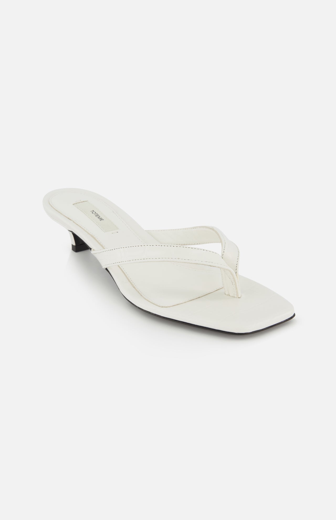 The TOTEME Croco Embossed Heeled Flip Flops feature white croc-embossed leather, a square toe, low black heel, and Italian craftsmanship, shown on a white background.