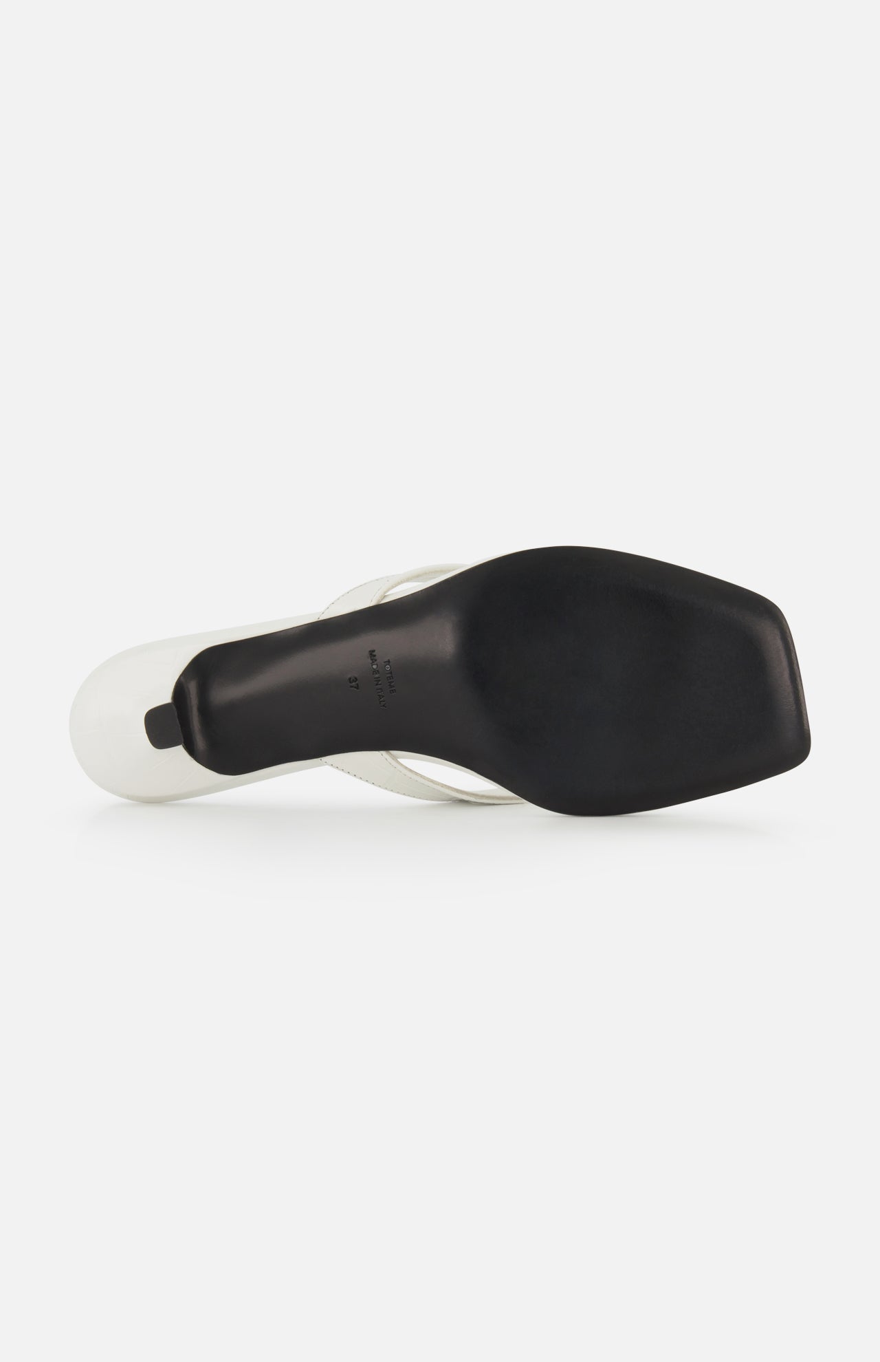 Bottom view of TOTEME’s Croco Embossed Heeled Flip Flops in white, featuring a black square-toed sole with a slightly raised heel and smooth finish. "Made in Italy" text is imprinted near the arch, showcasing its craftsmanship.