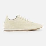 A side view of TOTEME's Flex Suede Low Profile Sneakers in beige, featuring white laces and a light brown rubber sole, photographed on a plain white background—expertly crafted in Italy for timeless appeal.