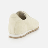 The Flex Suede Low Profile Sneakers by TOTEME feature beige minimalist suede uppers and light brown soles, viewed from the back/side. TOTEME is embossed on the heel. Made in Italy, shown against a white background.