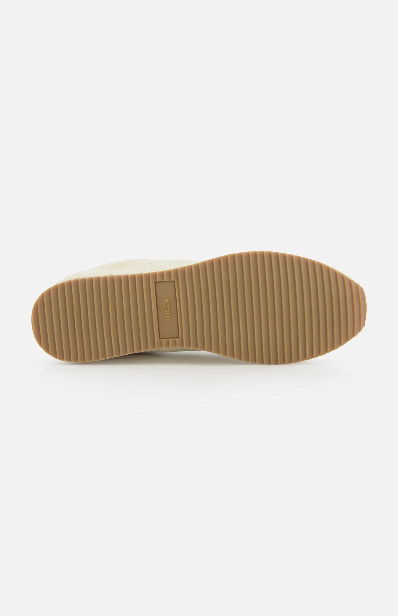 The image shows the bottom view of TOTEME's Flex Suede Low Profile Sneakers, made in Italy, with a tan ribbed rubber sole featuring horizontal grooves and a rectangular logo at the center, all set against a plain white background.
