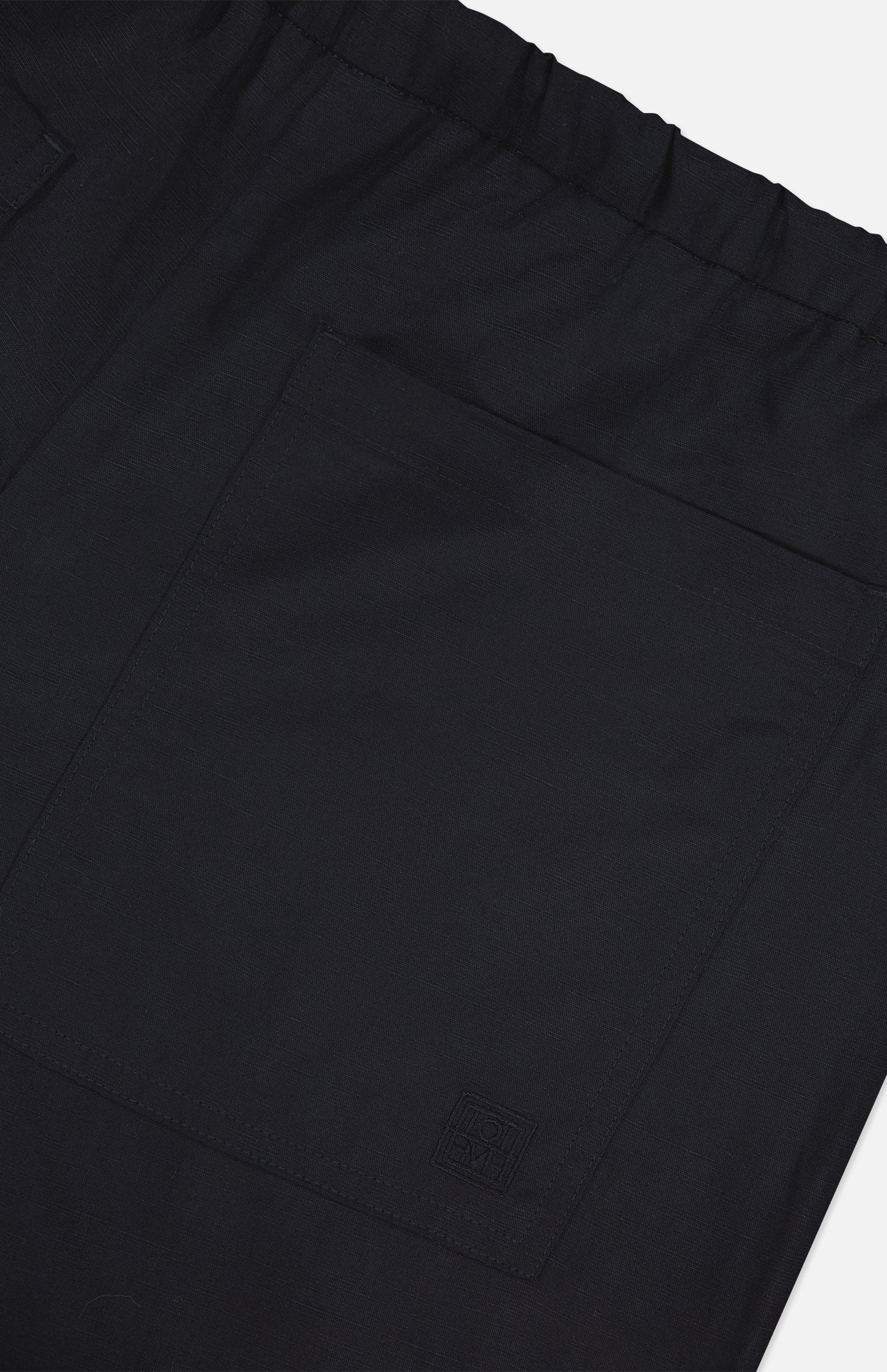 Close-up of TOTEME Fluid Drawstring Trouser Pants in black, featuring a comfy elastic waistband, large square side pocket, and a small stitched logo near the hem.