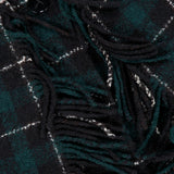 Close-up of the TOTEME Fringed Scarf Jacket, featuring a dark green and black plaid wool-blend fabric with white lines, black buttons, and fringed detailing. A white label with a geometric logo appears in the top left corner.