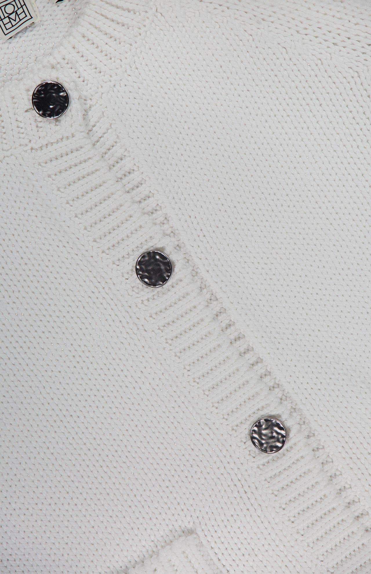 Close-up of the TOTEME Hammered Button Cotton Cardigan in white, featuring four hammered silver buttons and ribbed edges. The button-front closure lends classic appeal, with a portion of the label visible at the top left corner.