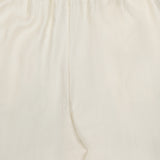 Close-up of TOTEME's Monogram Silk PJ Bottoms: cream-colored straight-leg pants featuring an elastic waistband, subtle stitching, and a delicate embroidered monogram on smooth silk fabric.