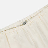 Close-up of the waistband on TOTEME's Monogram Silk PJ Bottoms, featuring cream-colored pleated silk, an elastic band, and a small fabric label sewn inside.