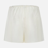 TOTEME Monogram Silk PJ Shorts shown against a white background. These cream silk shorts feature an elastic waistband, loose relaxed fit, minimal detailing, and an elegant embroidered monogram.