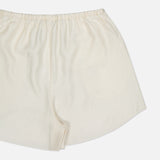 A close-up of TOTEME's Monogram Silk PJ Shorts in cream, made from lightweight silk with an elastic waistband and subtle embroidered monogram, shown on a white background.