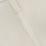 Close-up of TOTEME's Open-Front Bouclé Blazer in off-white, showing textured fabric with a visible seam and raw edge. A partially open slit reveals the smooth, lighter inner lining.