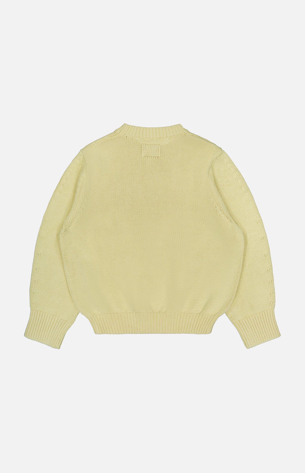An Oversized Crewneck Knit Sweater by TOTEME in butter yellow is laid flat with the back side facing up, showcasing long sleeves and ribbed detailing on the cuffs, waistband, and neckline against a plain white background.