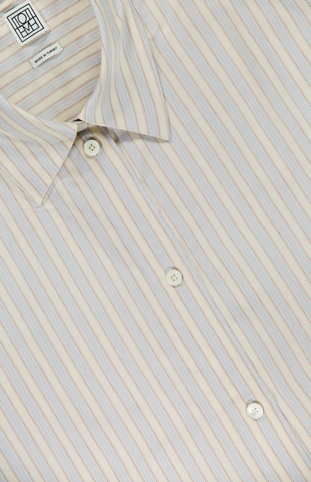 The TOTEME Oversized Pastel Striped Shirt features thin vertical stripes in light blue and brown on beige, a classic collar, and white front buttons for a timeless yet relaxed style.