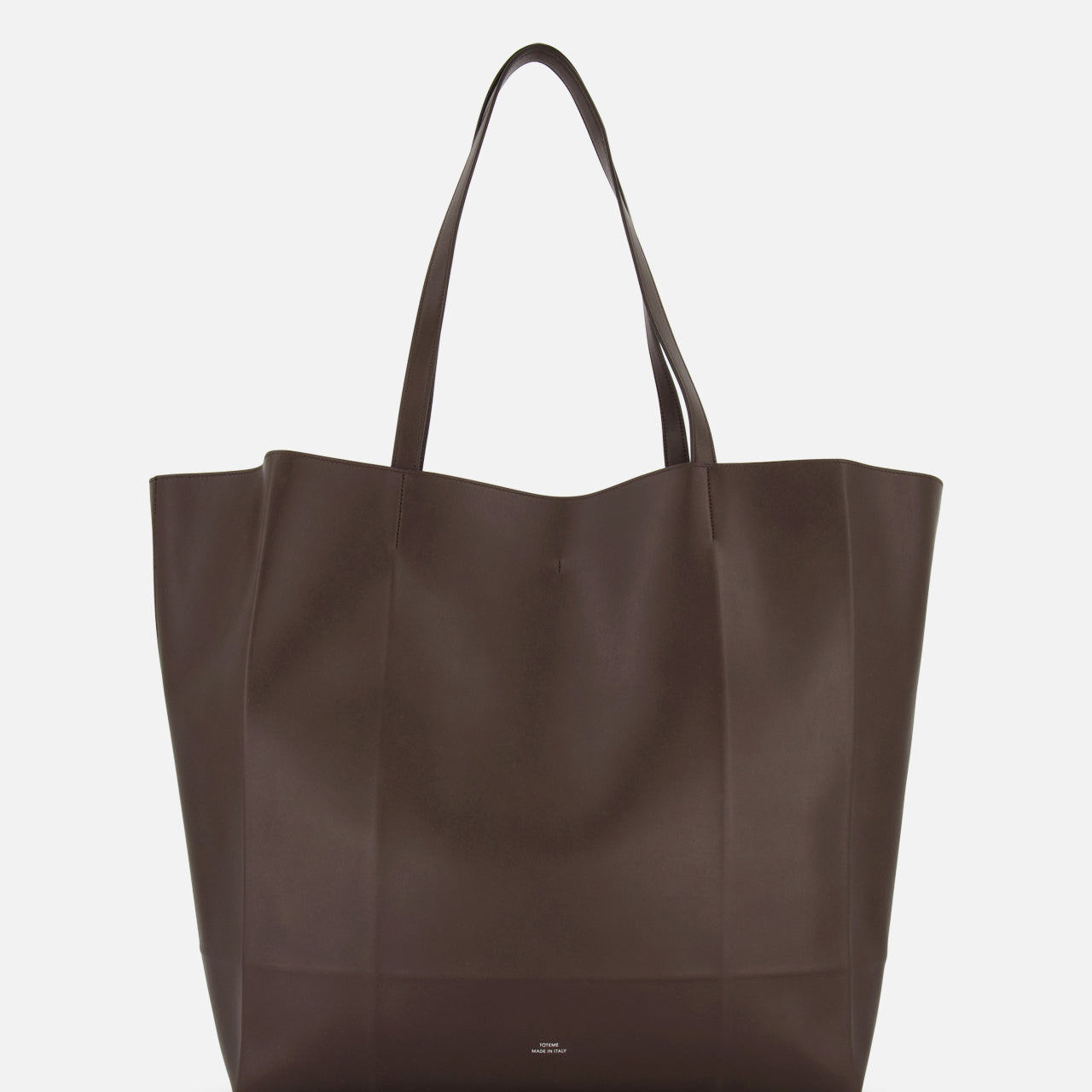 The TOTEME Roam Oversized Leather Tote Bag is shown against a white background. This large, dark brown bag has two handles and a minimalist design with no visible embellishments.
