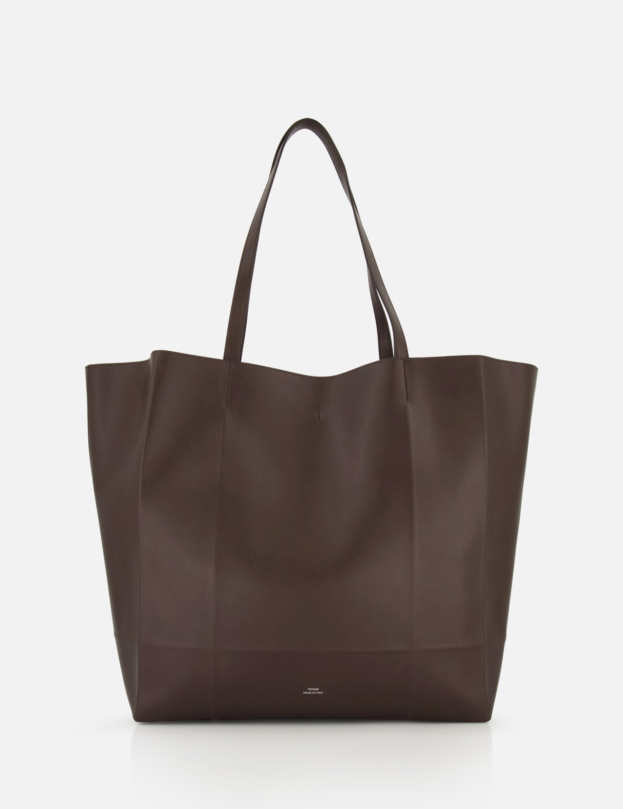 The TOTEME Roam Oversized Leather Tote Bag is shown against a white background. This large, dark brown bag has two handles and a minimalist design with no visible embellishments.