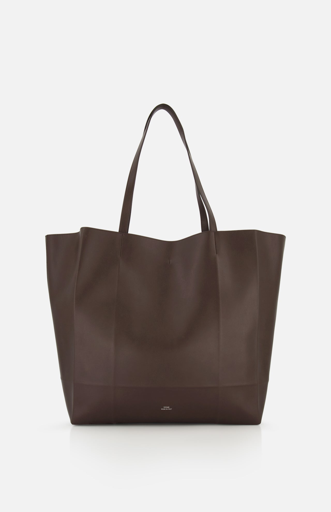 The TOTEME Roam Oversized Leather Tote Bag is shown against a white background. This large, dark brown bag has two handles and a minimalist design with no visible embellishments.