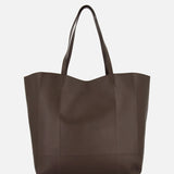 The TOTEME Roam Oversized Leather Tote Bag, made in Italy, features a minimalist dark brown design with two handles and an oversized silhouette, displayed against a plain white background.