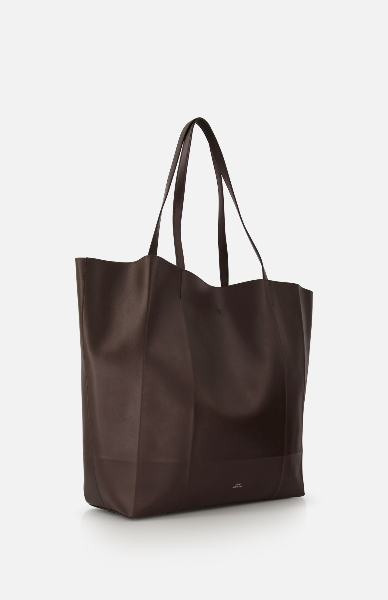 The TOTEME Roam Oversized Leather Tote Bag is a large, dark brown tote with two handles and a minimalist, slightly structured shape, displayed against a plain white background.
