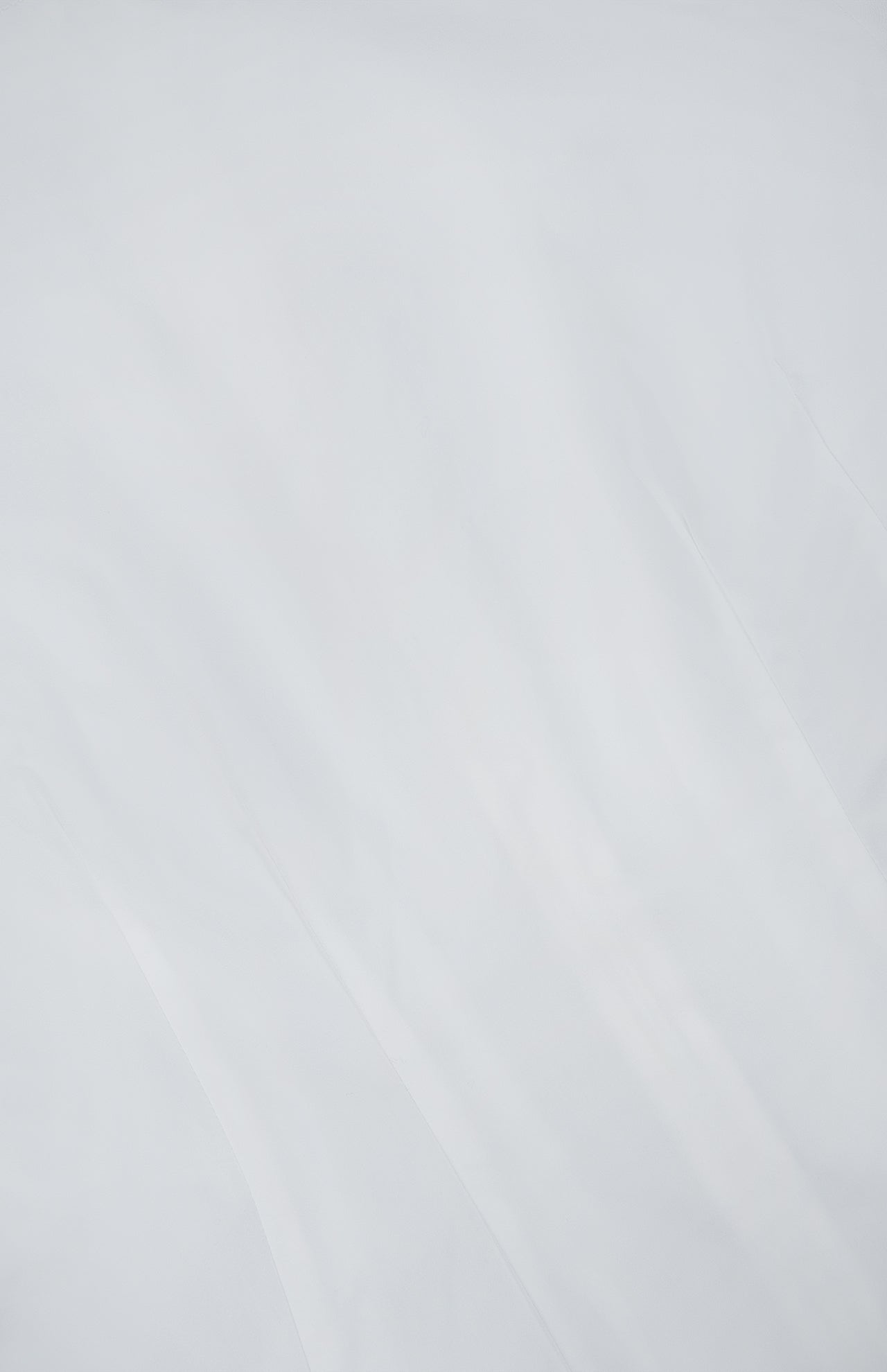 A close-up of the smooth, slightly wrinkled white cotton fabric from TOTEME’s Sculptural Cotton Top, with soft shadows highlighting the gentle folds and creases that lend this designer piece its refined, textured elegance.