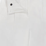 The TOTEME Single Pleat Cotton Trouser Pants feature a crisp, smooth cotton fabric and a white tailored silhouette. The partially open waistband reveals a black button and part of the zipper area, emphasizing their refined, modern design.
