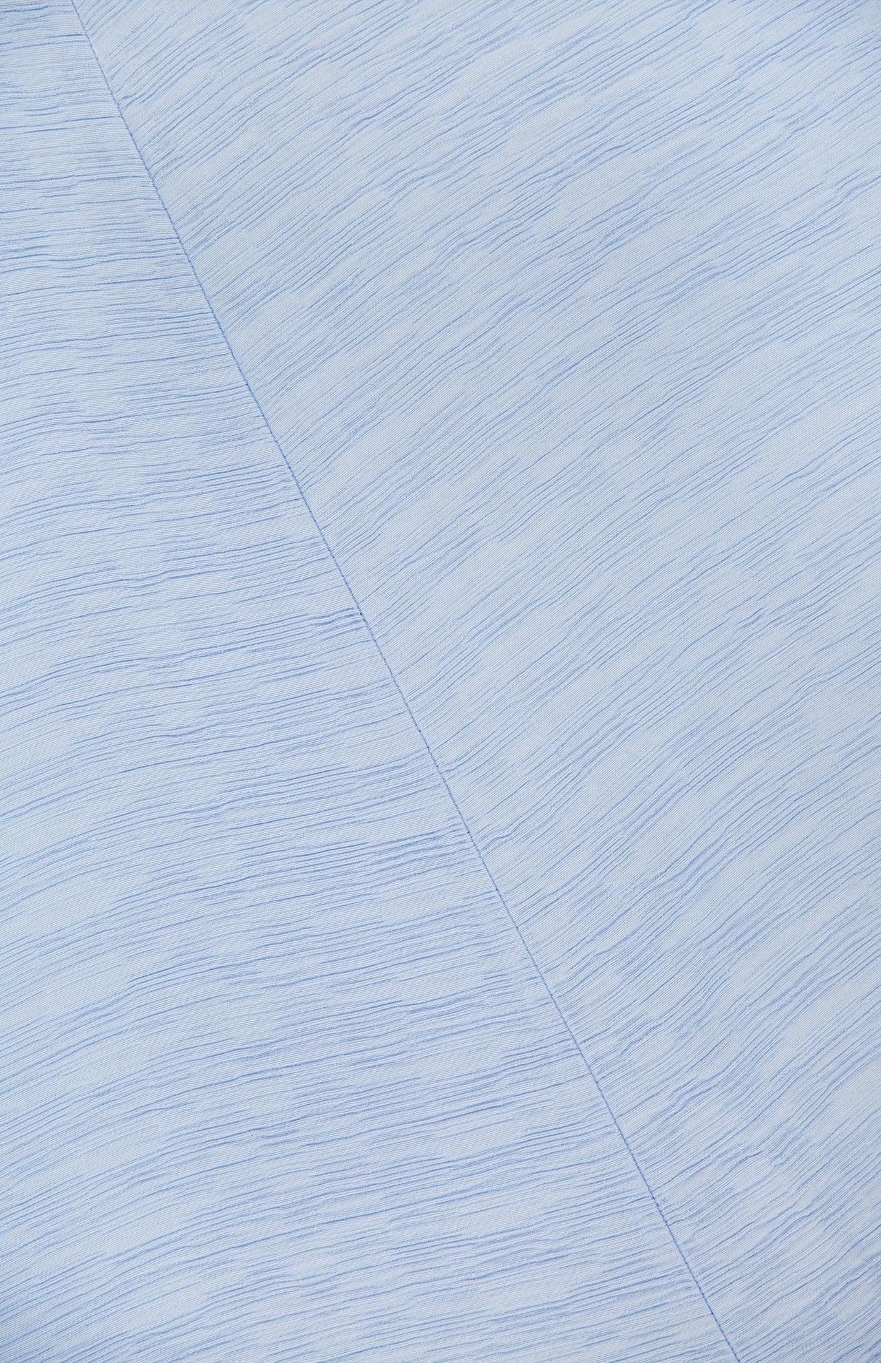 Close-up of the Slouch Waist Dress by TOTEME shows pale blue fabric with fine horizontal textured lines, a diagonal seam, and subtle blue variations—highlighting the elegant style and curved panel design.