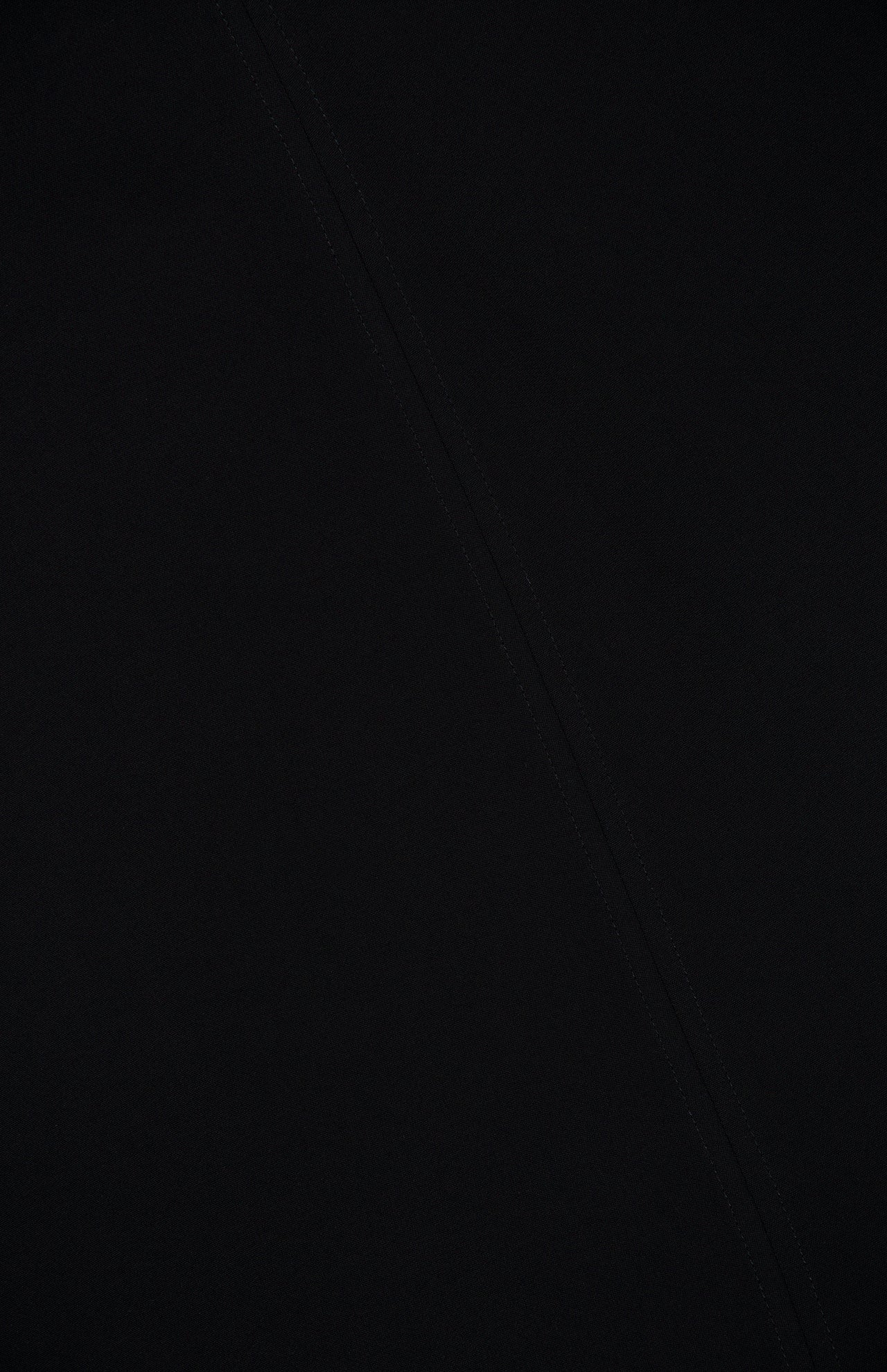 A close-up of the black fabric from TOTEME’s Slouch Waist Scarf Dress, featuring a subtle diagonal seam. The material is smooth, and the stitching blends seamlessly into the dark textile.