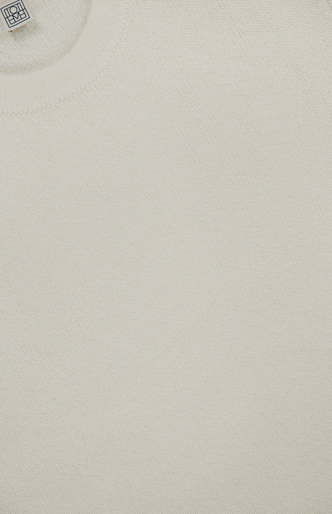 Close-up of the TOTEME Structured Crew Neck Knit Sweater in off-white, featuring a visible round neckline and a small white woven label near the collar.