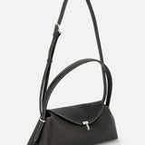 The TOTEME T-Lock Grained Leather Shoulder Bag features black pebble-grained leather, white stitching, a flap closure with a silver buckle, and an adjustable strap. Photographed on a plain white background. Made in Italy.