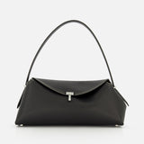 The TOTEME T-Lock Grained Leather Shoulder Bag, made in Italy from black pebble-grained leather, features a single curved strap, silver-tone hardware, and a front flap closure. Shown against a plain white background.