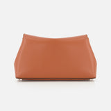 The TOTEME T-Lock Grained-Leather Clutch Bag is medium-sized and tan, featuring a soft, textured surface and a sculptural silhouette with a minimalist design. It's displayed against a plain white background.