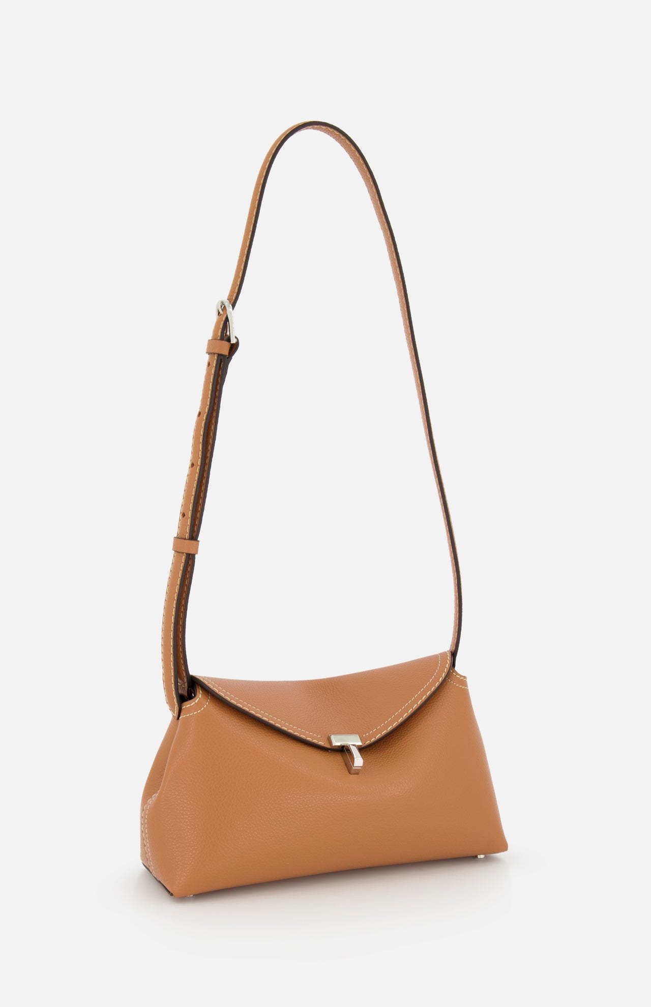 The TOTEME T-Lock Grained-Leather Clutch is a tan sculptural bag with a curved rectangular silhouette, adjustable strap, silver clasp, and white stitching, crafted in Italy and shown against a plain white background.