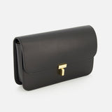 The TOTEME T-Lock Leather Crossbody Bag, featuring a sleek black leather finish and a gold rectangular clasp, is photographed on a white background, capturing the refined elegance of a sculptural silhouette and exuding the timeless sophistication of Italian-made accessories.
