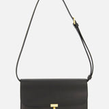 The TOTEME T-Lock Leather Crossbody Bag is a sculptural shoulder bag crafted from black leather in Italy, featuring a gold T-shaped clasp and an adjustable strap, displayed against a plain white background.