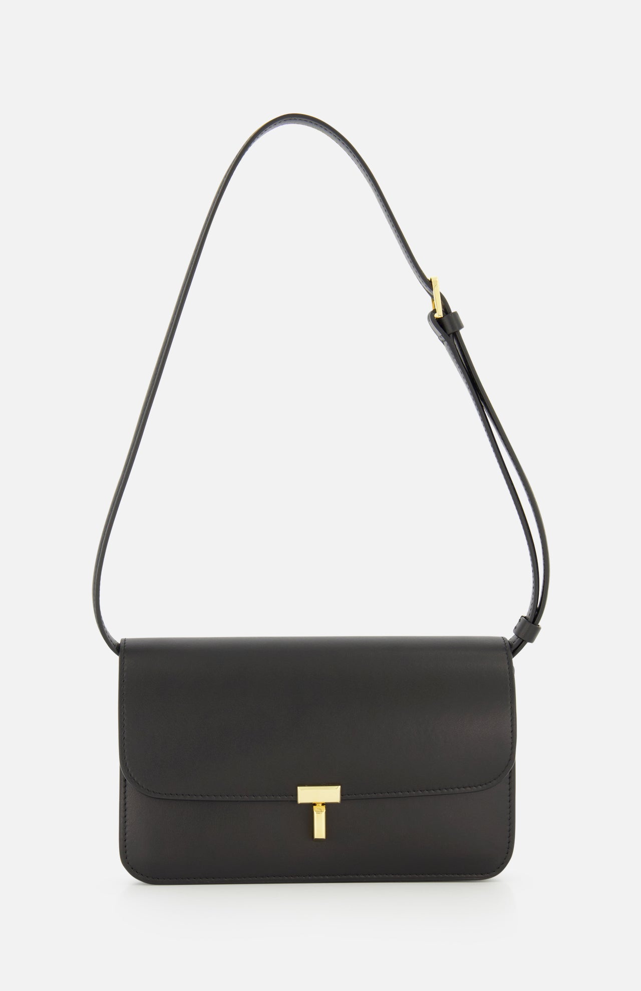 The TOTEME T-Lock Leather Crossbody Bag is a sculptural shoulder bag crafted from black leather in Italy, featuring a gold T-shaped clasp and an adjustable strap, displayed against a plain white background.