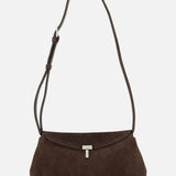 The TOTEME T-Lock Suede Clutch, crafted in chocolate brown suede with a long adjustable strap and finished with a silver clasp, made in Italy, is displayed on a plain white background.