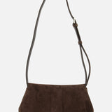 The TOTEME T-Lock Suede Clutch is a dark chocolate brown suede shoulder bag with a wide base, softly structured body, and an adjustable strap—crafted in Italy—and displayed against a plain white background.